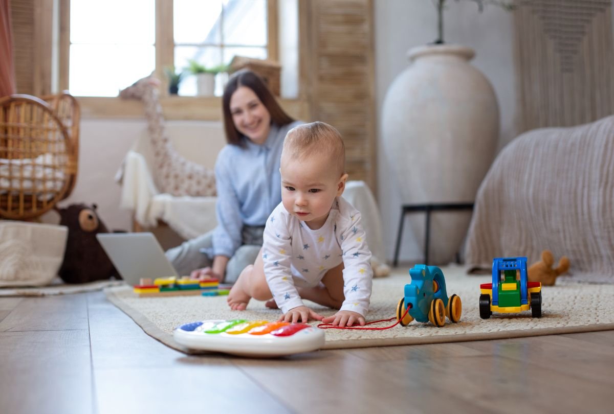 Dezvoltarea psihomotorie a sugarului  - sugar explorand jucarii pe covor, mama in fundal