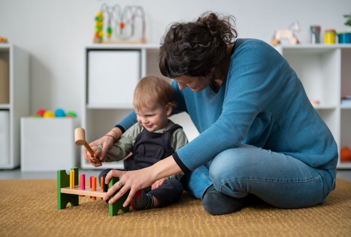 Dezvoltarea psihomotorie - baietel si mama se joaca cu o jucarie de lemn, cu ciocanel