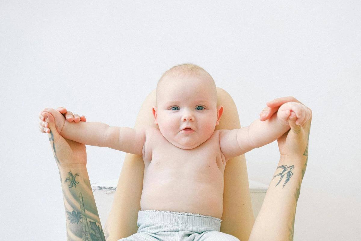 Ce mananca bebe la 8 luni-copil cu bratele intinse, maini cu tatuaje